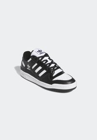 Black and white Adidas sneaker with three stripes on the side, black laces, and a white sole on a neutral background.