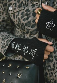 Černé bezprstové rukavice se stříbrnými hvězdnými ozdobami. Nosené s džískou s leopardím potiskem. Viditelná černá taška se zlatými akcenty.