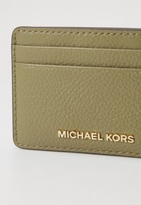 Portafoglio in pelle verde oliva con superficie texturizzata, quattro scomparti per carte e logo dorato "MICHAEL KORS" nell'angolo in basso a destra.