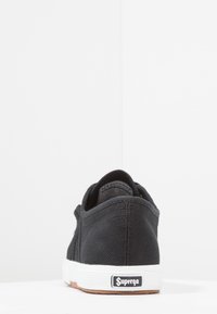 Schwarze Leinen-Sneaker mit weißer Gummisohle, ausgestattet mit einem strukturierten Obermaterial, glattem Fersenbereich und einem kleinen Superga-Logo auf der Rückseite.