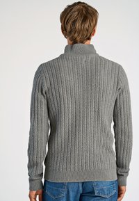 Szary, prążkowany sweter z wysokim kołnierzem, ozdobiony teksturowymi wzorami i dopasowanym w pasie. Połączony z niebieskimi dżinsami.