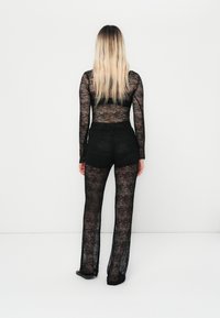 Black lace jumpsuit featuring long sleeves, fitted torso, and wide leg design. Sheer texture reveals skin beneath. No visible patterns or hardware.