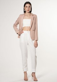 Blushroze blazer met een getailleerde pasvorm, gecombineerd met witte hoog-waisted broeken met opgerolde mouwen en knoopaccenten. Soepele texturen.