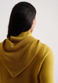 Mosterdgele capuchontrui met geribbelde textuur, voorzien van een gedrapeerde capuchon en een driehoekige vorm aan de achterkant. Simpel ontwerp, casual pasvorm.