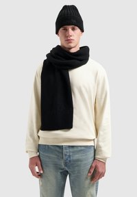 Zwarte geribbelde brei-muts en sjaal; zachte textuur. Draagt een lichtbeige sweatshirt en verwassen lichtblauwe spijkerbroek. Eenvoudig, functioneel ontwerp.