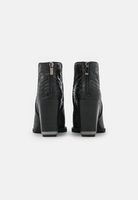 Botines negros hechos de cuero con estampado de serpiente texturizado, que presentan una cremallera trasera y tacones gruesos con un acento plateado en la base.