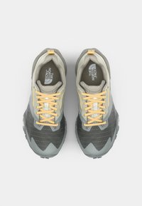 Gray and beige sneakers with textured mesh upper, yellow laces, and a distinctive zigzag design on the sole. Logo on the tongue.
