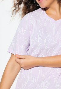 Camiseta de manga corta en color lavanda con un cuello redondo que presenta un diseño de dibujo continuo en línea blanca de varios animales a lo largo de la tela.