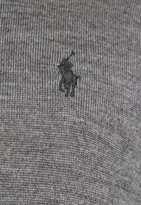 Grå stickad tröja med en texturerad design och en liten svart broderad polo-spelare logotyp. Slät tyg med ett subtilt mönster.