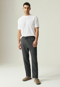 Un t-shirt en coton blanc, un pantalon gris à cordon et des chaussures brunes à enfiler se dressent contre un fond neutre. Le pantalon est fabriqué dans un tissu léger.