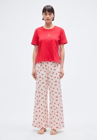 T-shirt rouge en coton à manches courtes, assorti à un pantalon large rose clair avec un motif cerises. Tissu doux, coupe décontractée, sans accents.