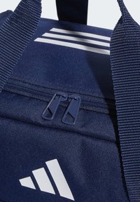 Marineblauwe stoffen sporttas met een wit logo met drie strepen, dubbele ritssluiting en een gestructureerde geweven handgreep. Compact en stevig ontwerp.