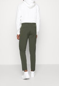 Pantaloni verde oliva a taglio aderente realizzati in un tessuto morbido, caratterizzati da una texture liscia e due tasche posteriori, abbinati a sneaker bianche.