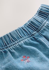 Blåt denimstof med elastisk taljebånd og lille pink og rød broderet blomsterdesign nær syningen.