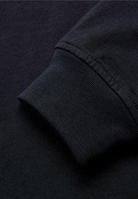 Černá bavlněná košile s dlouhým rukávem, látka s žebrovaným manžetovým zakončením. Hladká textura, jednoduchý design a jemné šití.