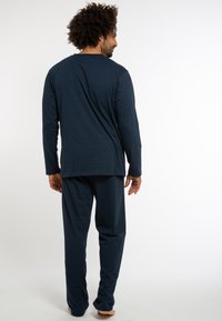 Mørkeblå afslapningstøj i blødt stof, med lange ærmer og bukser i en afslappet pasform, synlige sømme og en subtil tekstur.