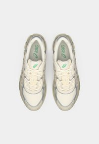 Baskets en maille blanche et synthétique grise avec des accents verts, dotées d'une semelle épaisse, d'un laçage et d'un logo bien en vue sur la languette.