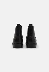 Botas de tobillo de cuero negro con un acabado suave, paneles elásticos en los laterales y un tacón bajo apilado; marca mínima en la parte trasera.