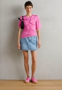 Pink ruched top, denim mini skirt, pink sneakers with green accents, black handbag, and hoop earrings. Smooth textures and casual design.