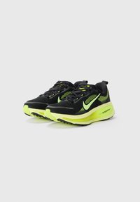 Chaussures de sport noires avec une tige texturée, des accents vert fluo et une semelle épaisse. Comprend un design rembourré pour le soutien et la traction.