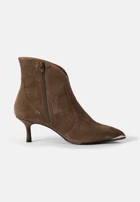 Botine din suede maro, cu vârf ascuțit, detaliu cu fermoar pe lateral și un toc mic, conic. Textură netedă și linii curate.