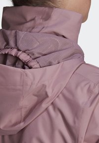 Světlounce růžová bunda s nazbíranou kapucí vybavenou síťovanou podšívkou pro ventilaci. Hladká textura s jemnými šicími detaily.