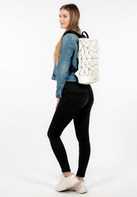 Witte rugzak met geometrisch patroon, gemaakt van synthetisch materiaal, met een oprolsluiting en zwarte banden, getoond op een model.