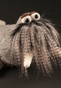 Plush toy resembling a walrus, gray body with textured fur, large round eyes, and a prominent, long striped mustache. White tusks.