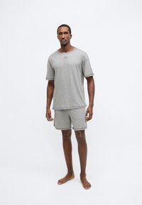 Σετ από γκρι βαμβακερή μπλούζα με κοντά μανίκια και σορτς, με άνετη εφαρμογή και αντίθετη λεπτομέρεια. Διαθέτει μικρό λογότυπο στο στήθος.