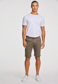 Witte crew-neck t-shirt gecombineerd met bruine shorts met omgeslagen mouwen. De shorts hebben een gestructureerde stof en worden gedragen met witte sneakers.