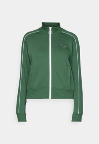 Vihreä vetoketjullinen takki, jossa on valkoiset sivuraidat, korkea kaulus ja etutaskut. Rinnassa on Nike-logo, ja hihoissa ja helmassa on resorit.