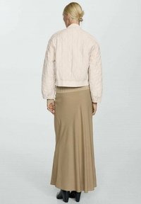 Quilted light pink bomber jacket, cropped design with ribbed hem, paired with a long beige skirt and black ankle boots. Back view.