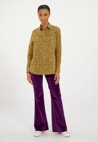 Chemise à boutons florale jaune, verte et rouge avec un col. Associée à un pantalon évasé violet et des baskets blanches. Look décontracté.