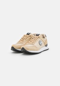 Sneakers atletiche beige con upper in mesh e camoscio, punta rotonda, chiusura con lacci e suola in gomma nera. Presentano un logo sul lato.