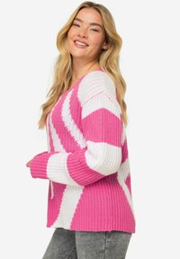 Stickad tröja i rosa och vita ränder, med V-ringning och långa ärmar. Texturerat tyg med ribbade muddkragar och fåll.