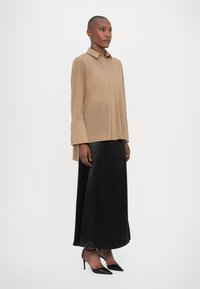 Beige long-sleeve shirt with a collar, paired with a high-waisted black satin skirt and black pointed-toe heels. Smooth textures throughout.
