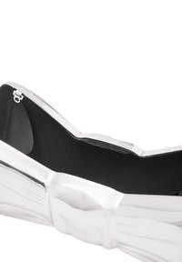 Metaliczna srebrna torebka w kształcie kokardy, z teksturowanym wykończeniem na zewnątrz i gładką czarną podszewką wewnątrz.