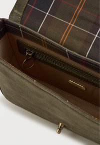 Olive zöld suede pénztárca belseje kockás bélésel, barna, piros és narancssárga színben. Zipzáros zsebet és egy arany logós címkét tartalmaz.