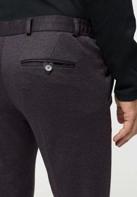 Close-up of a person wearing dark purple tailored pants with a buttoned back pocket and a black long-sleeve top.