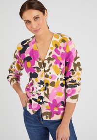 Cardigan multicolore avec des motifs floraux roses, jaunes et noirs. Texture côtelée, col en V et fermeture à boutons. Coupe décontractée avec des manches longues.