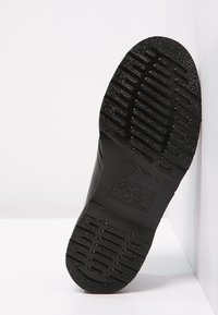 Suola di scarpa in gomma nera con texture antiscivolo, caratterizzata da costole e un logo impresso sul tallone. Design piatto e robusto.