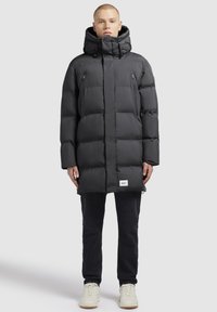 Must must lasekott, millel on kapuuts, varustatud lukuga taskute ja sildiga allääres. Valmistatud sujuvast, isoleeritud kangast, millel on kastitaoline lõige.