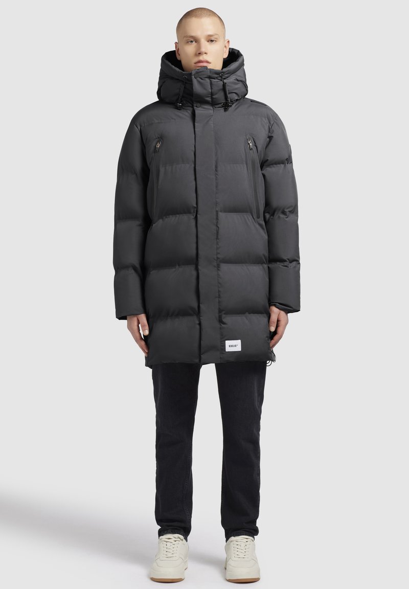 Must must lasekott, millel on kapuuts, varustatud lukuga taskute ja sildiga allääres. Valmistatud sujuvast, isoleeritud kangast, millel on kastitaoline lõige.