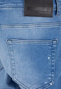 Light blue denim jeans feature a back pocket with a subtle white paint splatter. Includes a black label with "2Y PREMIUM" embossed.