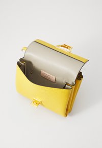 Borsa a tracolla gialla in pelle con una finitura texturizzata, dotata di una chiusura dorata e di un interno grigio. Include un'etichetta del marchio all'interno.