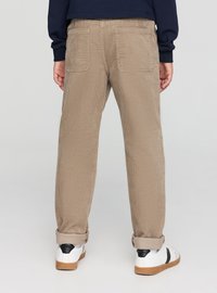 Pantaloni in velluto a coste color marrone chiaro, con due tasche posteriori, taglio dritto e risvolti, abbinati a scarpe da ginnastica bianche.