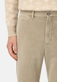 Beige kordtrotter med vertikala ränder, med en framfick och bältesöglor. Fästa med en märkesknapp i midjan.