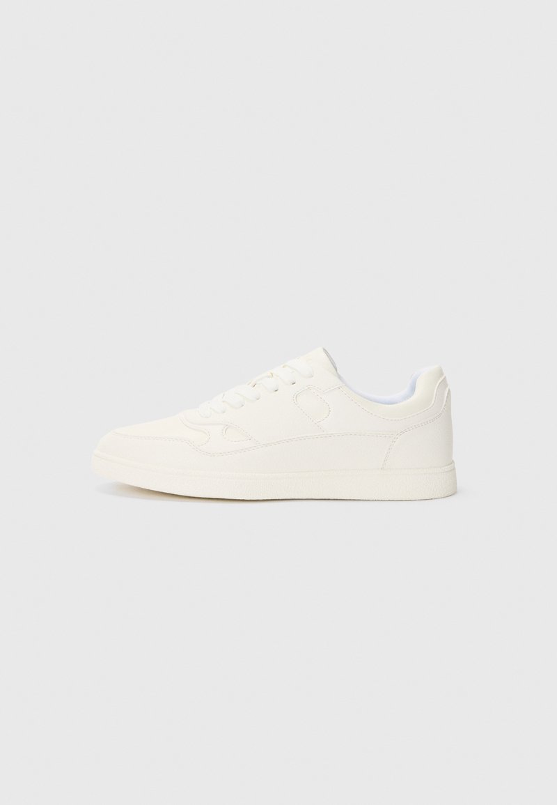 Valged sneaksid, millel on siledast nahast ülemine osa, ümar nina, lame tald ja toniseeritud õmblused. Omab nööbitavat esiosa ja peent brändingu detaili.