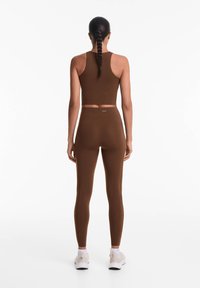 Barna sportos felszerelés, amely egy cropped tank topból és magas derekú leggingsből áll. Simács, rugalmas anyag, testhezálló fazonnal.