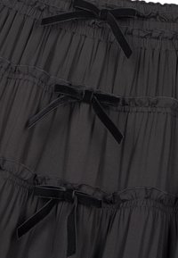 Tissu noir froncé avec trois rangées horizontales de nœuds en velours noir espacés régulièrement, créant un motif décoratif superposé.